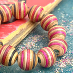 Red, pink, black and teal skateboard maple beads, chunky bracelet leaning on a worn red deck.