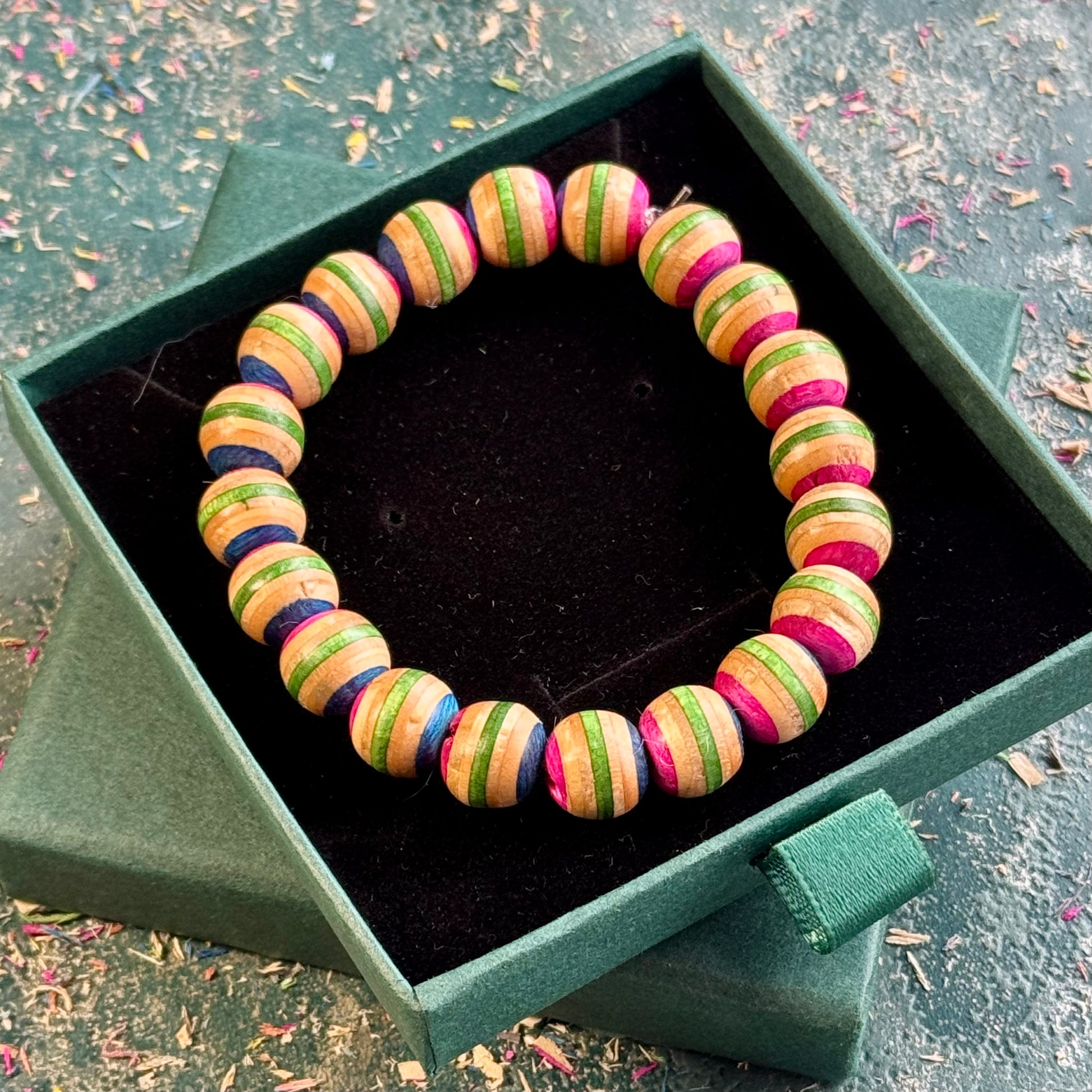Pink and green beaded bracelet made from recycled skateboard maple, shown from above in its box