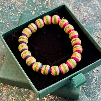Pink and green beaded bracelet made from recycled skateboard maple, shown from above in its box