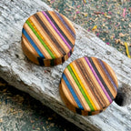 Wooden ear plugs with blue, purple, orange and green stripes across the face, cut from a recycled skateboard.