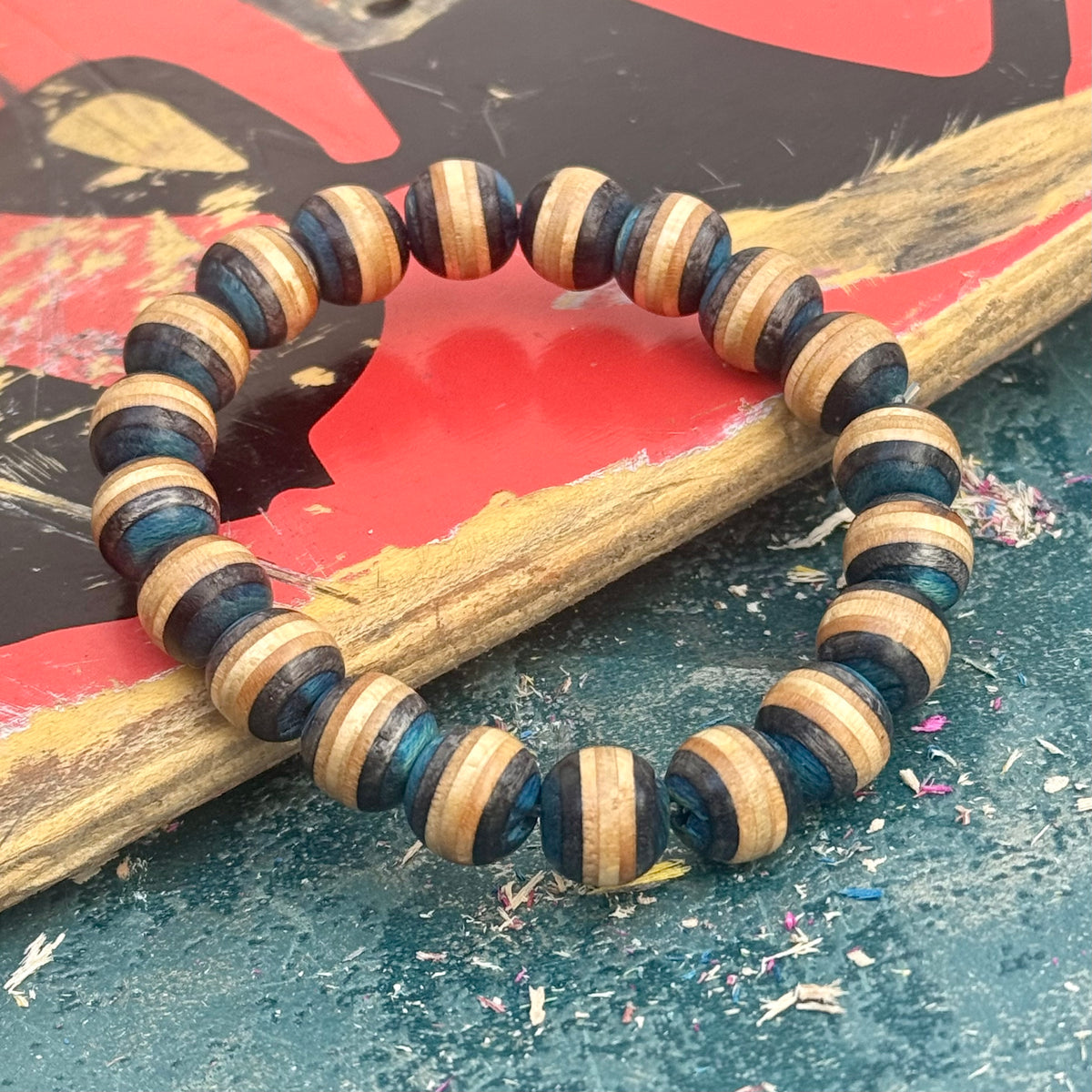 Blue and black wood bead bracelet in a full round on a painted skateboard deck, handmade by Baltic Dew.