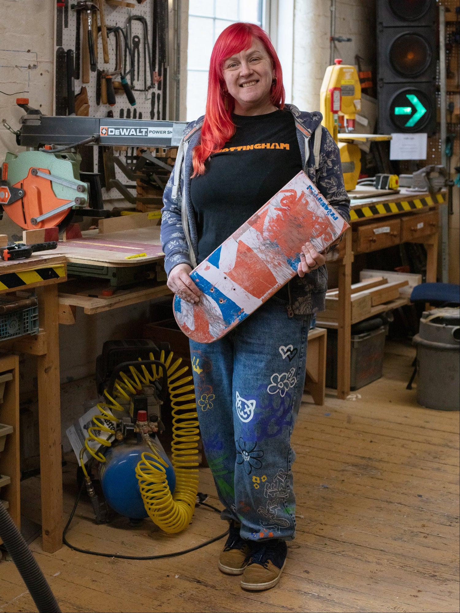Person with red hair holding a skateboard in a workshop