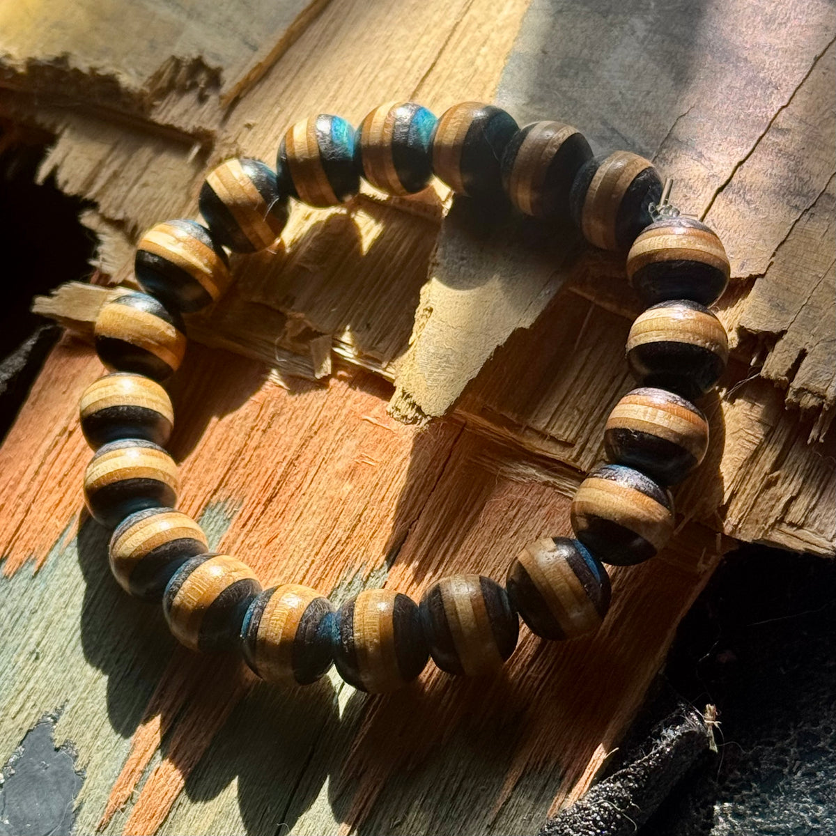 Blue and black wood bead bracelet from recycled skateboard maple lying on split, weathered plywood.