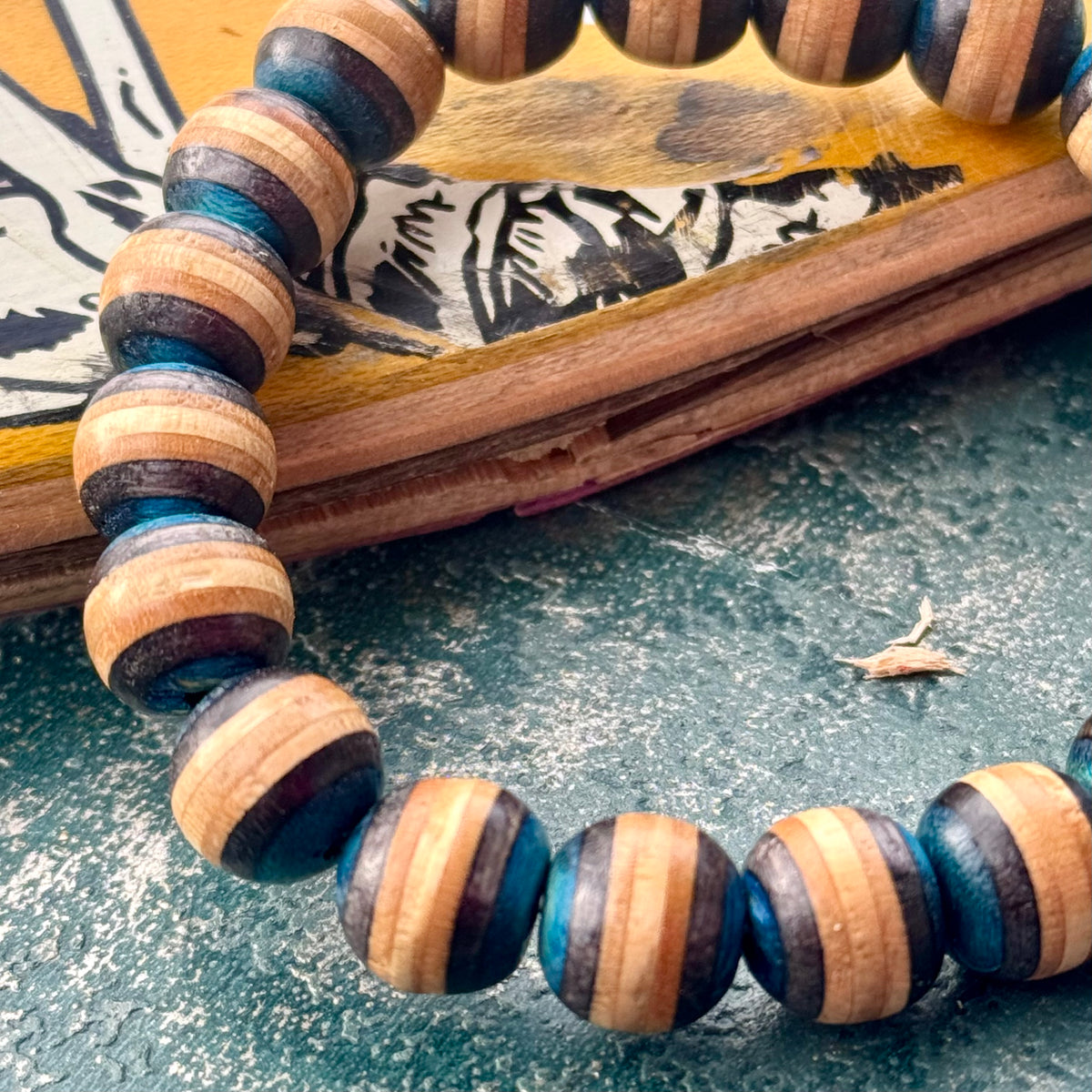 Close-up of blue and black layers on beads cut from a recycled skateboard deck, resting on a yellow printed deck.