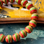 Recycled skateboard maple beads in red, green and teal, bracelet leaning on a worn deck edge.