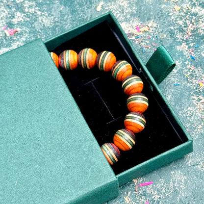 Recycled skateboard wood bracelet in orange, green and red, lying in an open gift box, handmade by Baltic Dew.