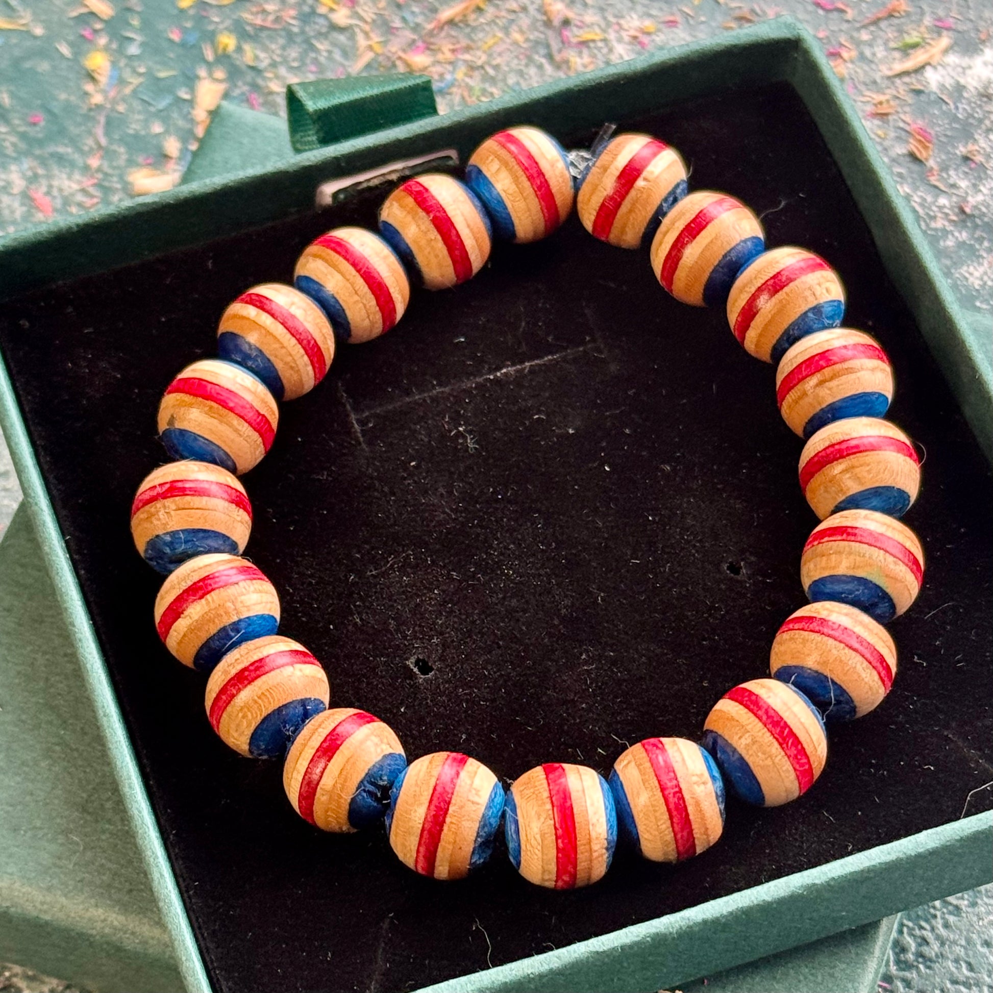 Blue and red recycled skateboard wood bead bracelet resting in its green gift box