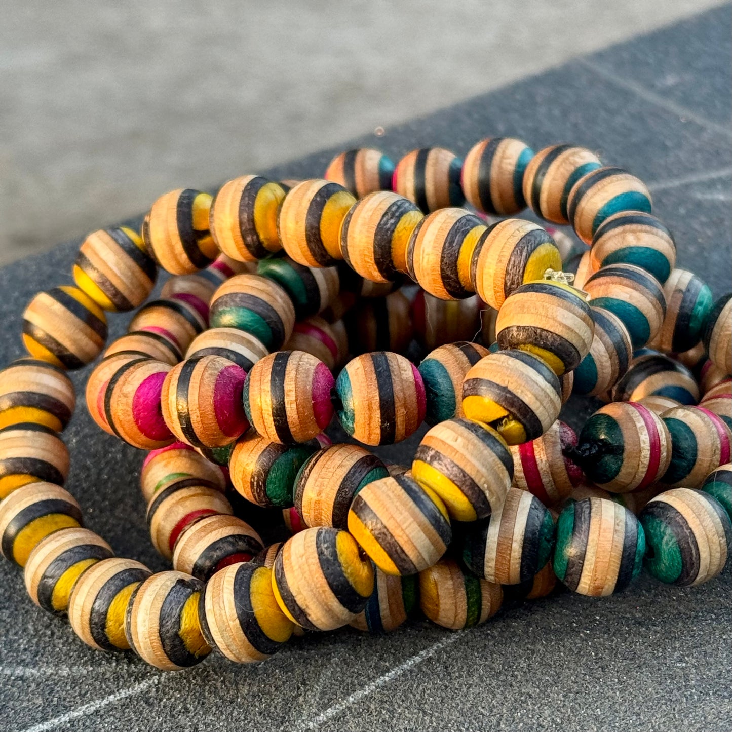 Three recycled skateboard wood beaded bracelets stacked together, showing the different colourways