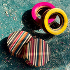Pink and yellow skateboard wood tunnels beside two striped plugs cut across the deck layers.