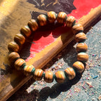 Light teal and yellow wood bead bracelet from recycled skateboard maple, laid in a full round on a painted deck.