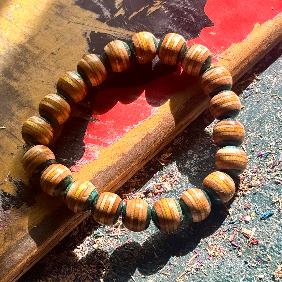 Light teal and yellow wood bead bracelet from recycled skateboard maple, laid in a full round on a painted deck.