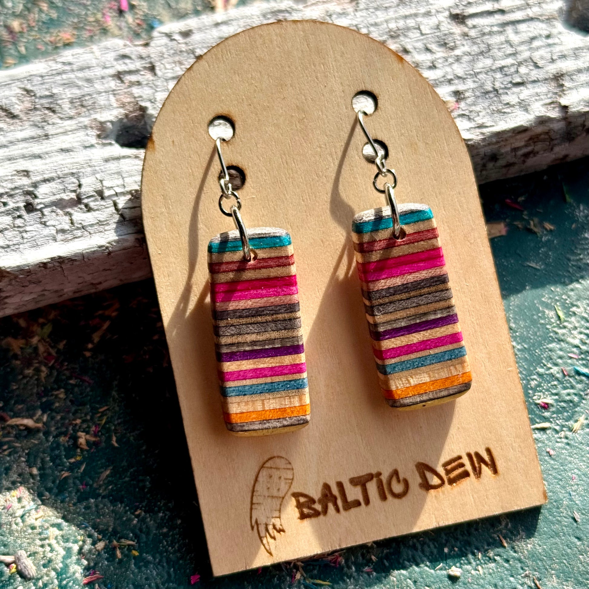 Slim striped skateboard wood drop earrings in teal, pink and purple, shown on a Baltic Dew card