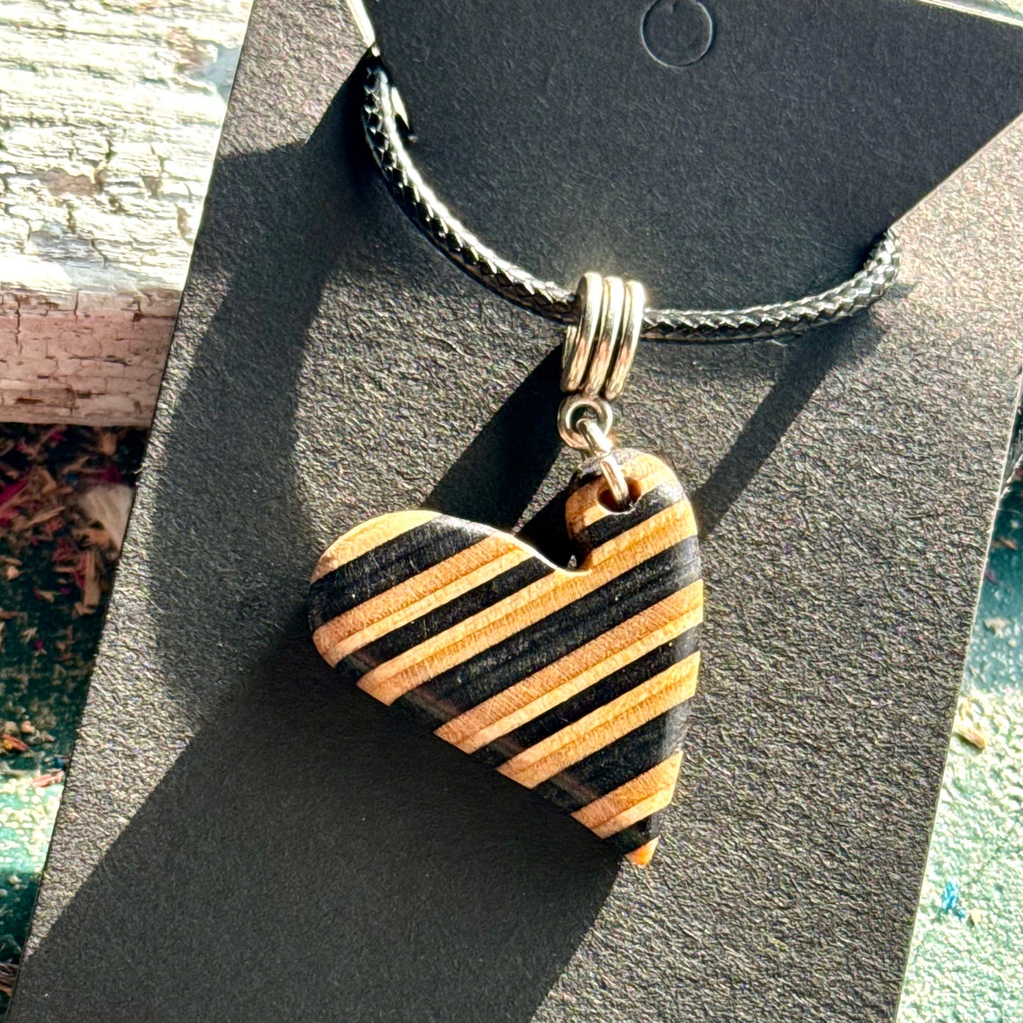 Black and natural striped wooden heart pendant cut from recycled skateboard maple on a waxed cord.