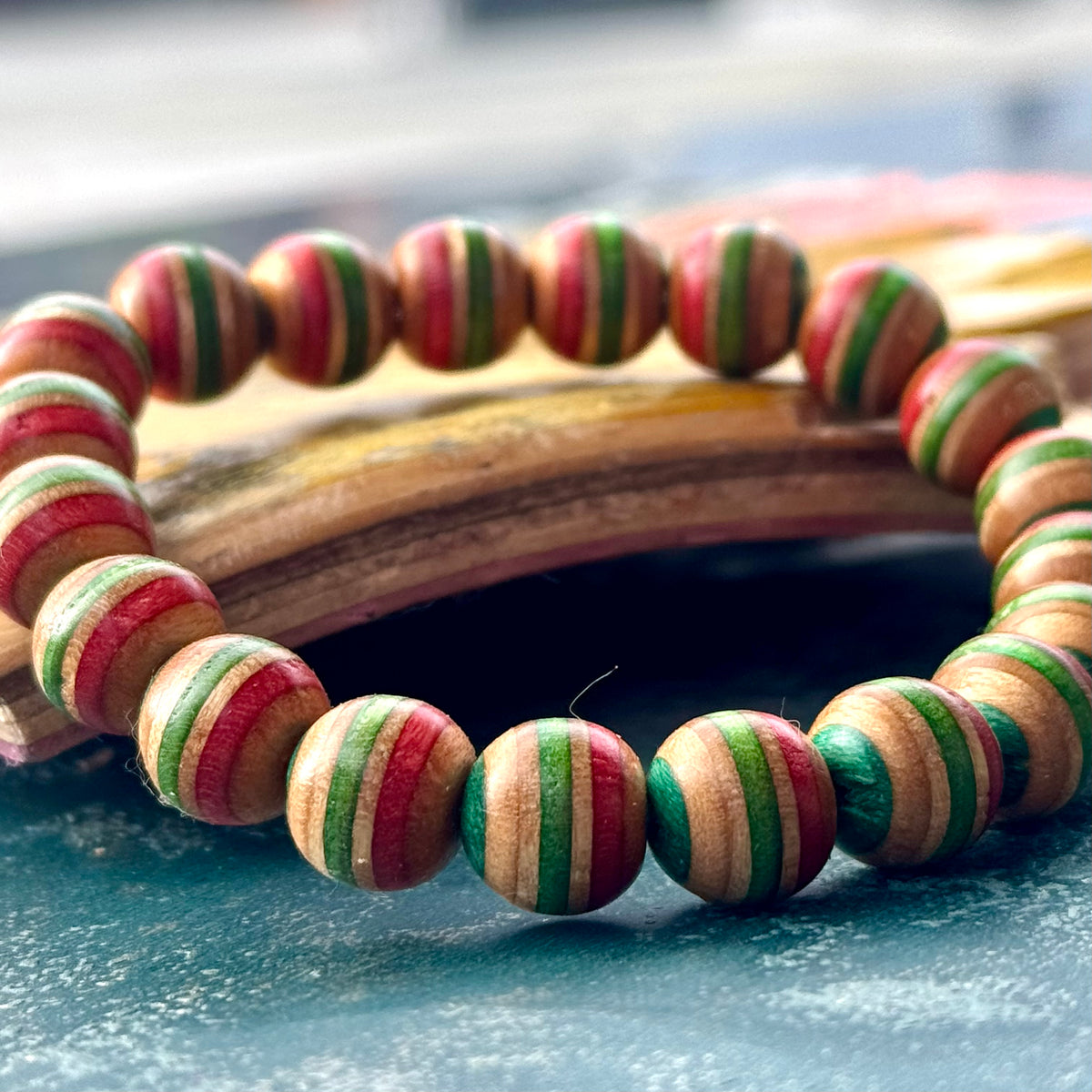 Red, green and teal striped beads from a recycled skateboard deck, shown at bead level in sunlight.