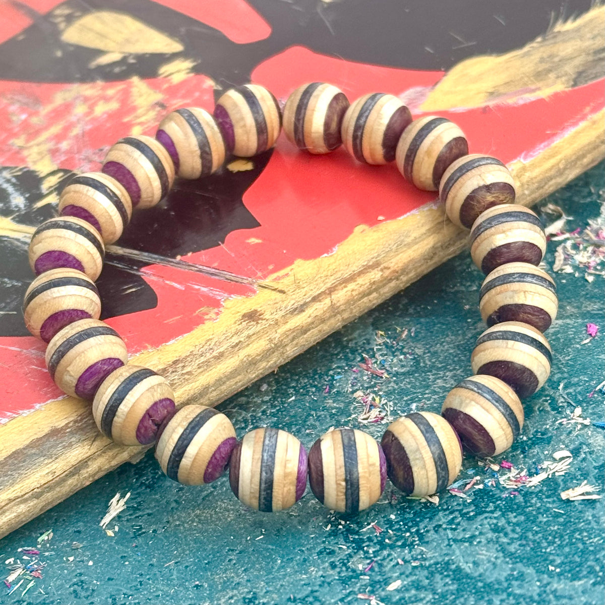 Brown, black and purple wood bead bracelet from recycled skateboard maple, laid in a full round on a red deck.