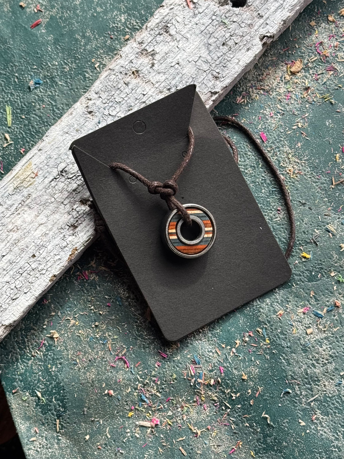 Skateboard bearing pendant with orange and natural maple layers on an adjustable waxed cotton cord.