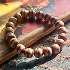 Brown, black and purple striped wooden bead bracelet in low sunlight on a painted skateboard deck.