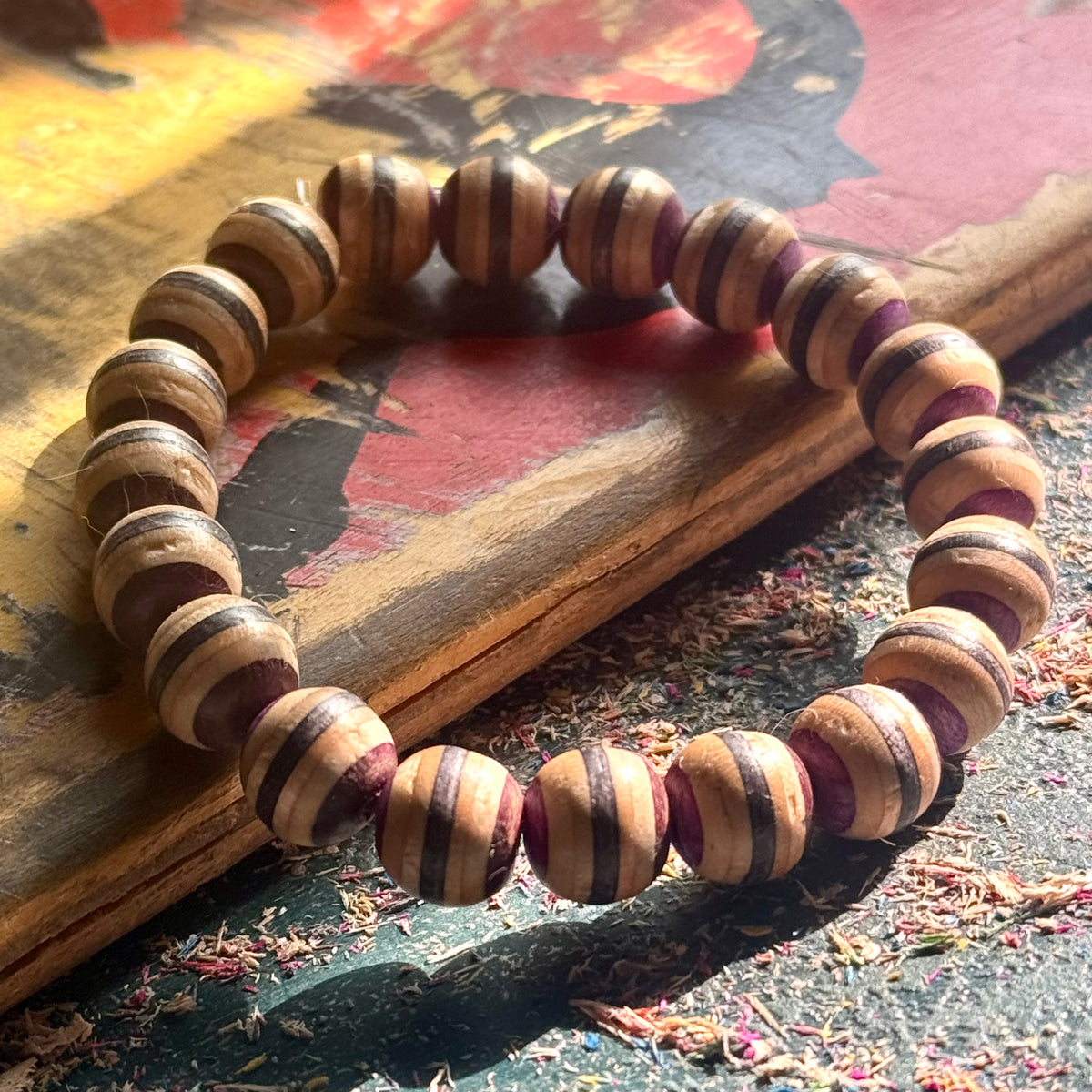 Brown, black and purple striped wooden bead bracelet in low sunlight on a painted skateboard deck.