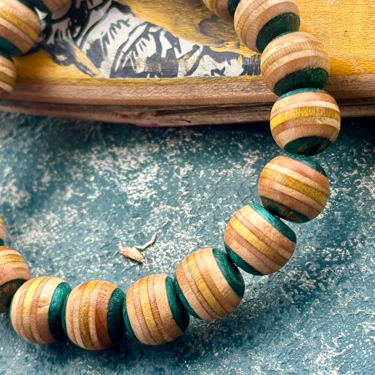 Light teal and yellow striped maple beads from a recycled skateboard deck, strung on elastic cord.