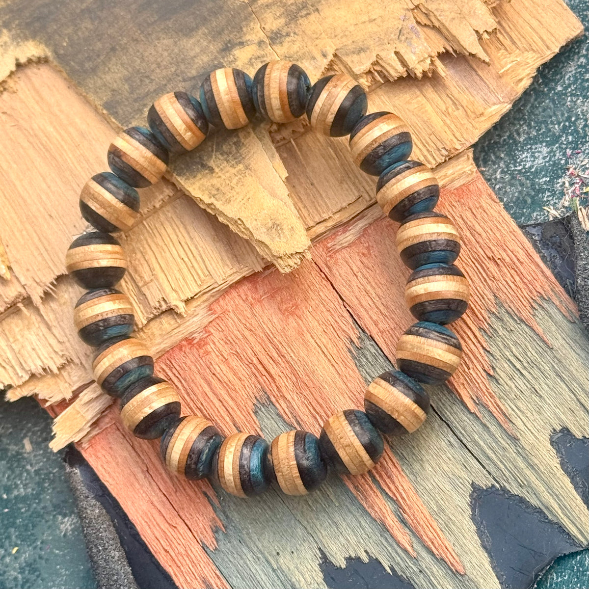 Blue and black recycled skateboard maple bracelet on cracked, layered wood, showing the full round.