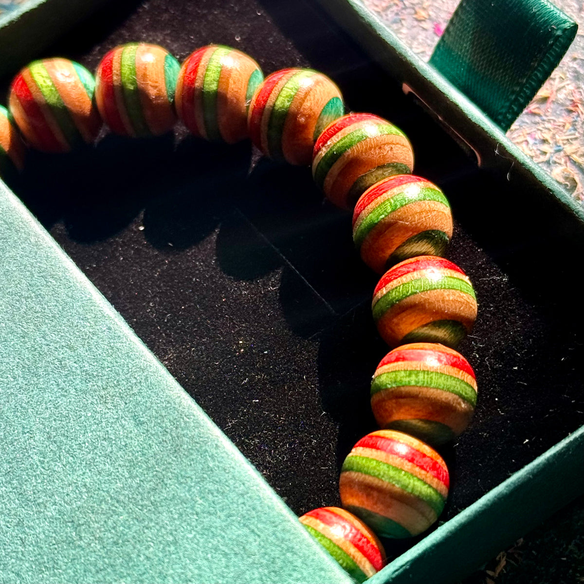 Red, green and teal recycled skateboard wood bead bracelet in its open green Baltic Dew gift box.