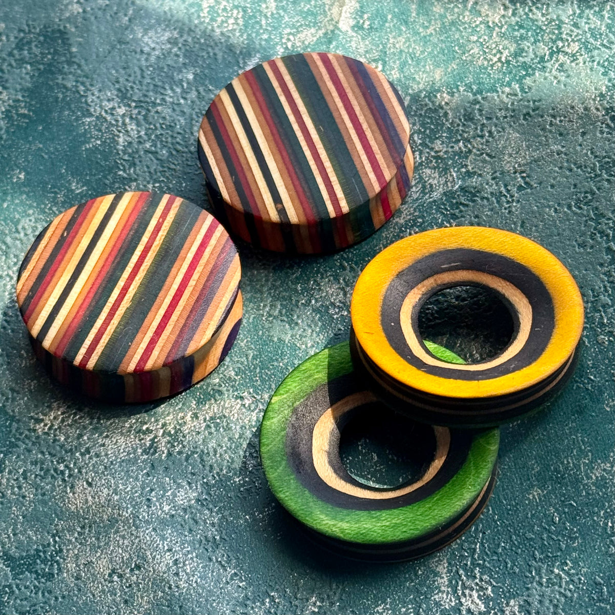 Striped plugs beside yellow and green tunnels, all cut from recycled skateboard maple.