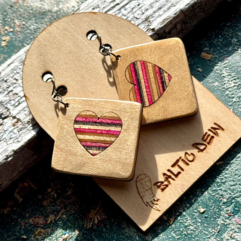 Beige recycled skateboard square drop earrings with heart cut-outs, showing pink, black and cream layered maple.