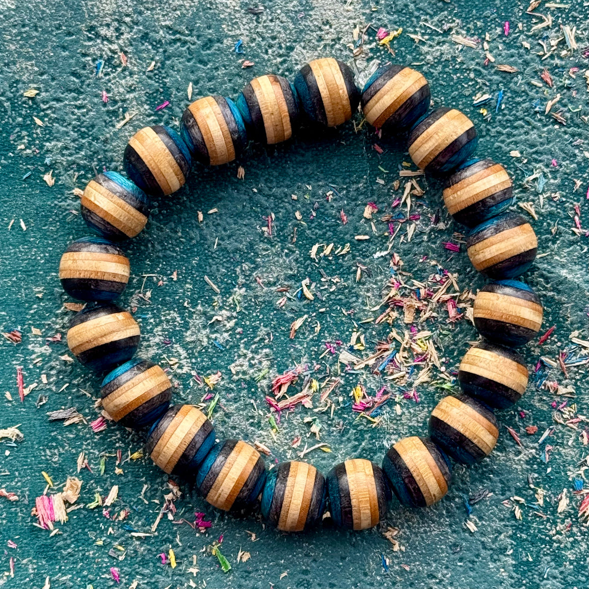 Blue and black recycled skateboard wood bead bracelet seen from above among colourful wood shavings.