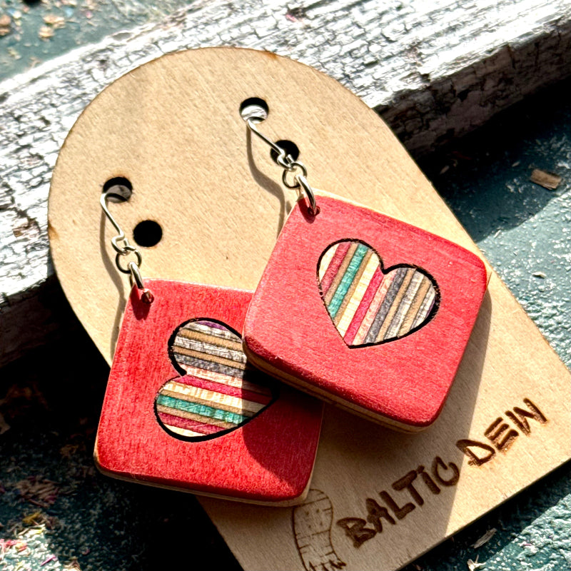 Red recycled skateboard square drop earrings with heart cut-outs, showing cream, orange and pink layered maple.