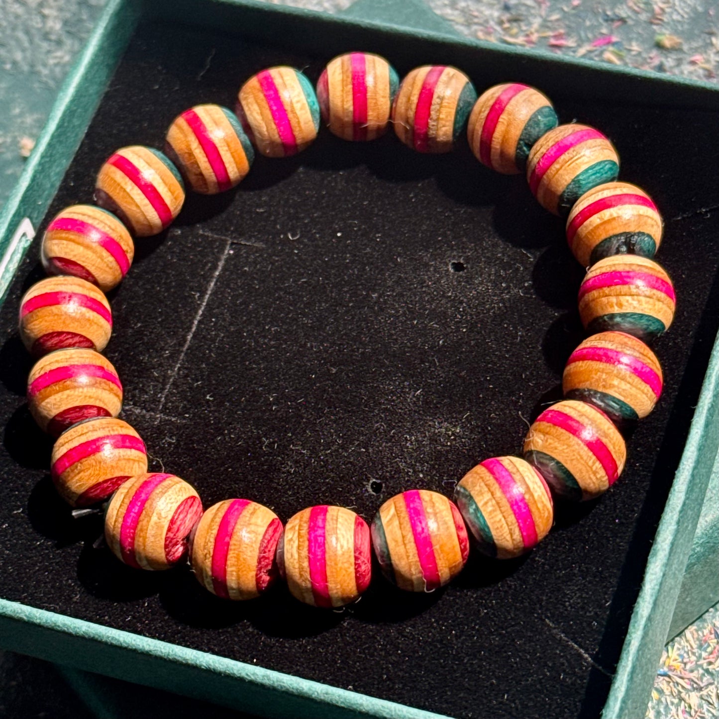 Pink and Teal Skateboard Bracelet featuring round wooden beads with alternating pink and teal stripes laid out in a black jewelry box.