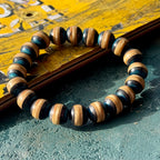 Blue and black recycled skateboard bracelet resting against a yellow deck with printed graphics, handmade by Baltic Dew.