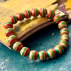 Red, green and teal wood bead bracelet from recycled skateboard maple resting on a weathered deck.