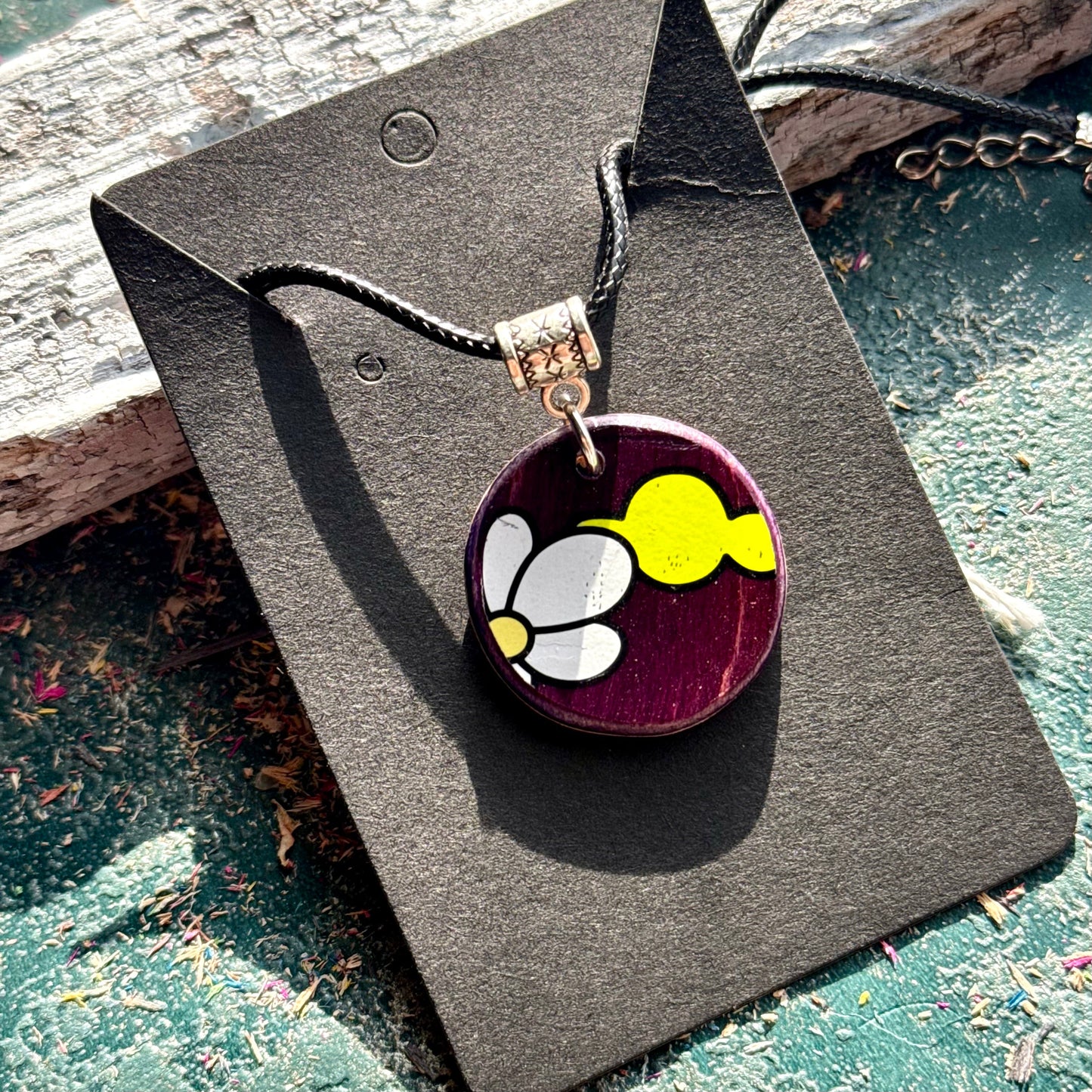 Purple recycled skateboard wood pendant with white petals and a yellow shape, handmade by Baltic Dew.