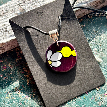 Purple recycled skateboard wood pendant with white petals and a yellow shape, handmade by Baltic Dew.
