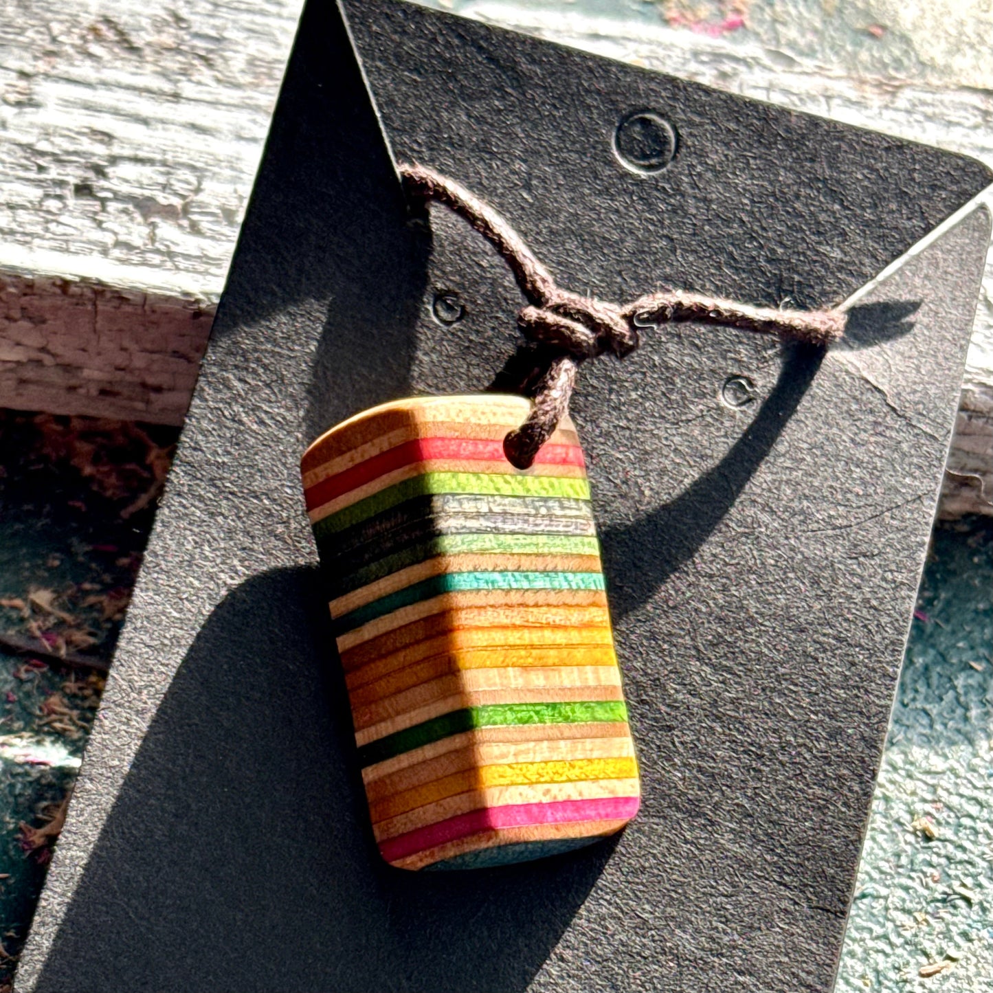 Rainbow striped wooden pendant cut from recycled skateboard maple on a brown waxed cord.