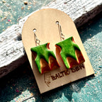 Carved wave earrings made from recycled skateboard maple, shown on a Baltic Dew card outdoors