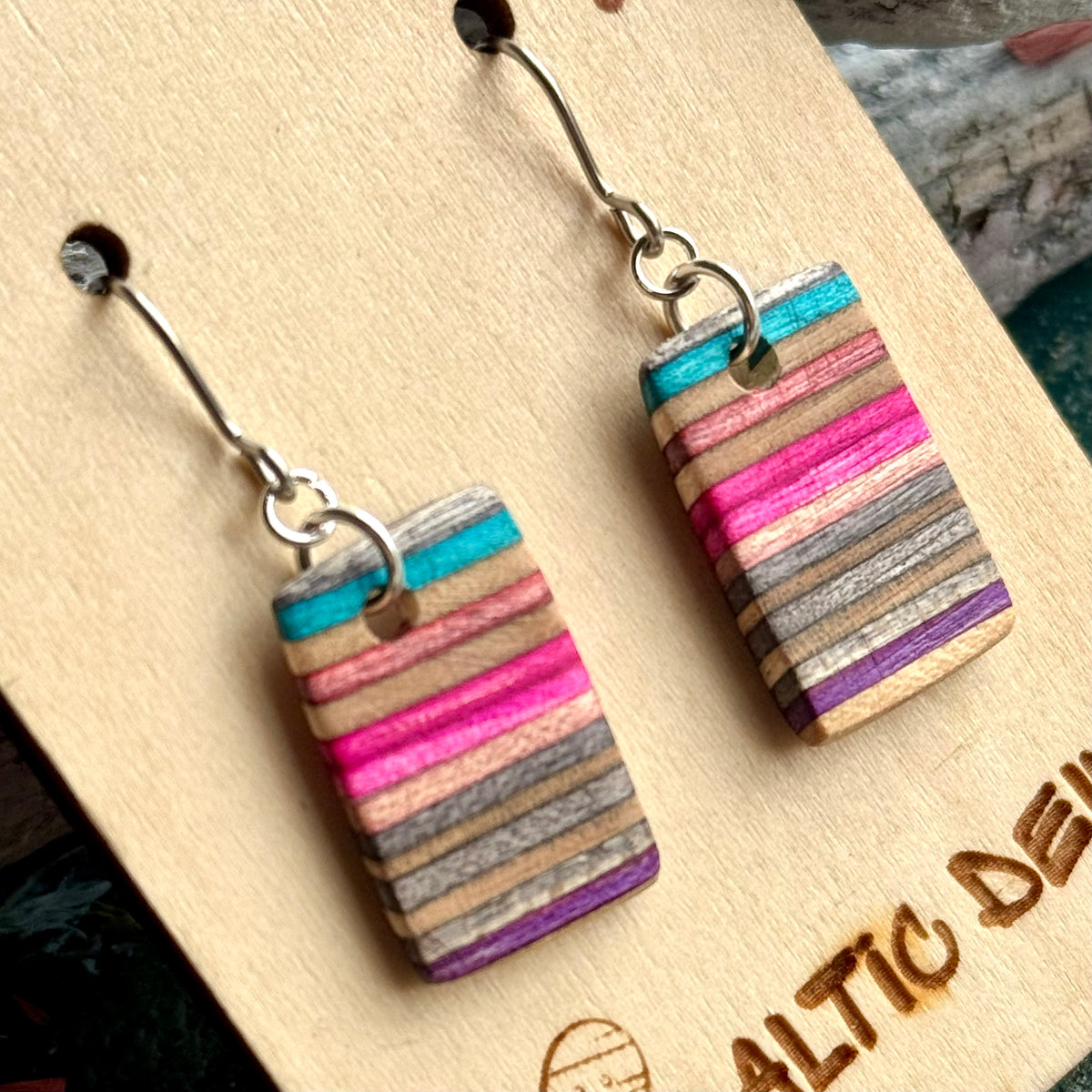 Close view of turquoise, pink, purple and grey layers striping a small skateboard wood earring