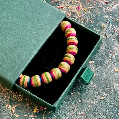 Pink and green recycled skateboard wood bead bracelet in its gift box, photographed outdoors