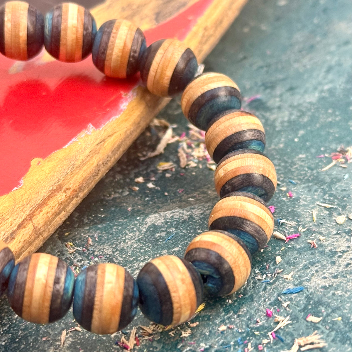 Blue and black beads from a recycled skateboard deck, the bracelet resting on a red deck.