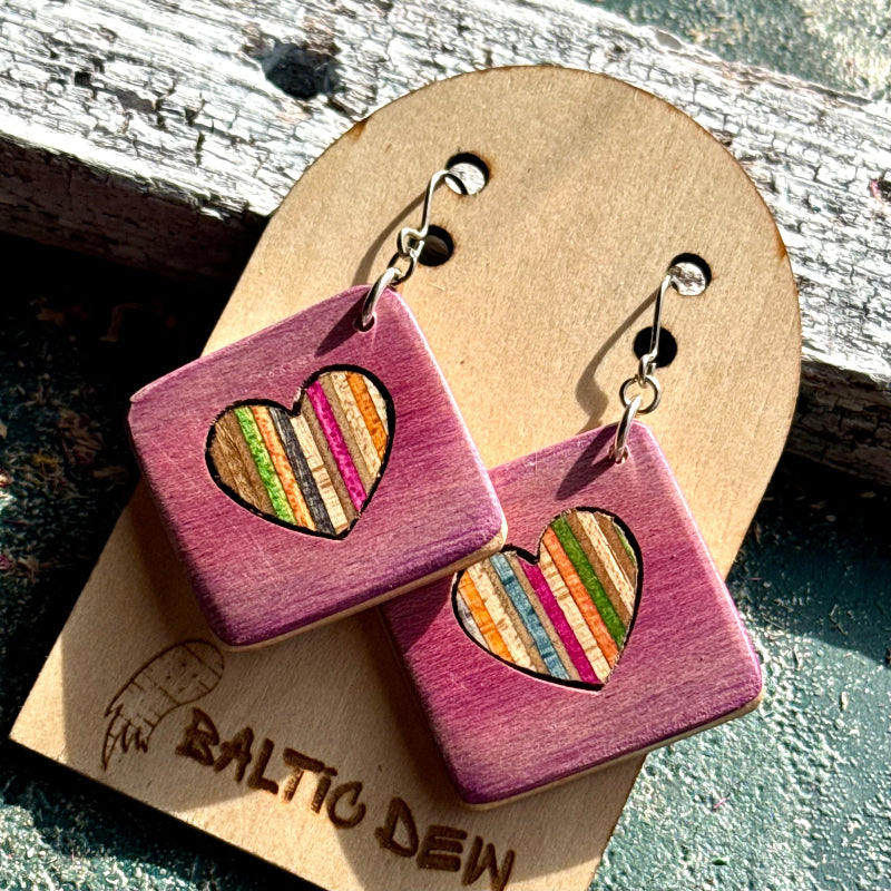 Pink recycled skateboard square drop earrings with heart cut-outs, showing layered maple colours.