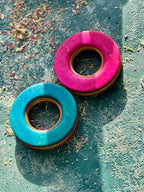 Pink and turquoise skateboard wood tunnels resting on a textured teal surface.