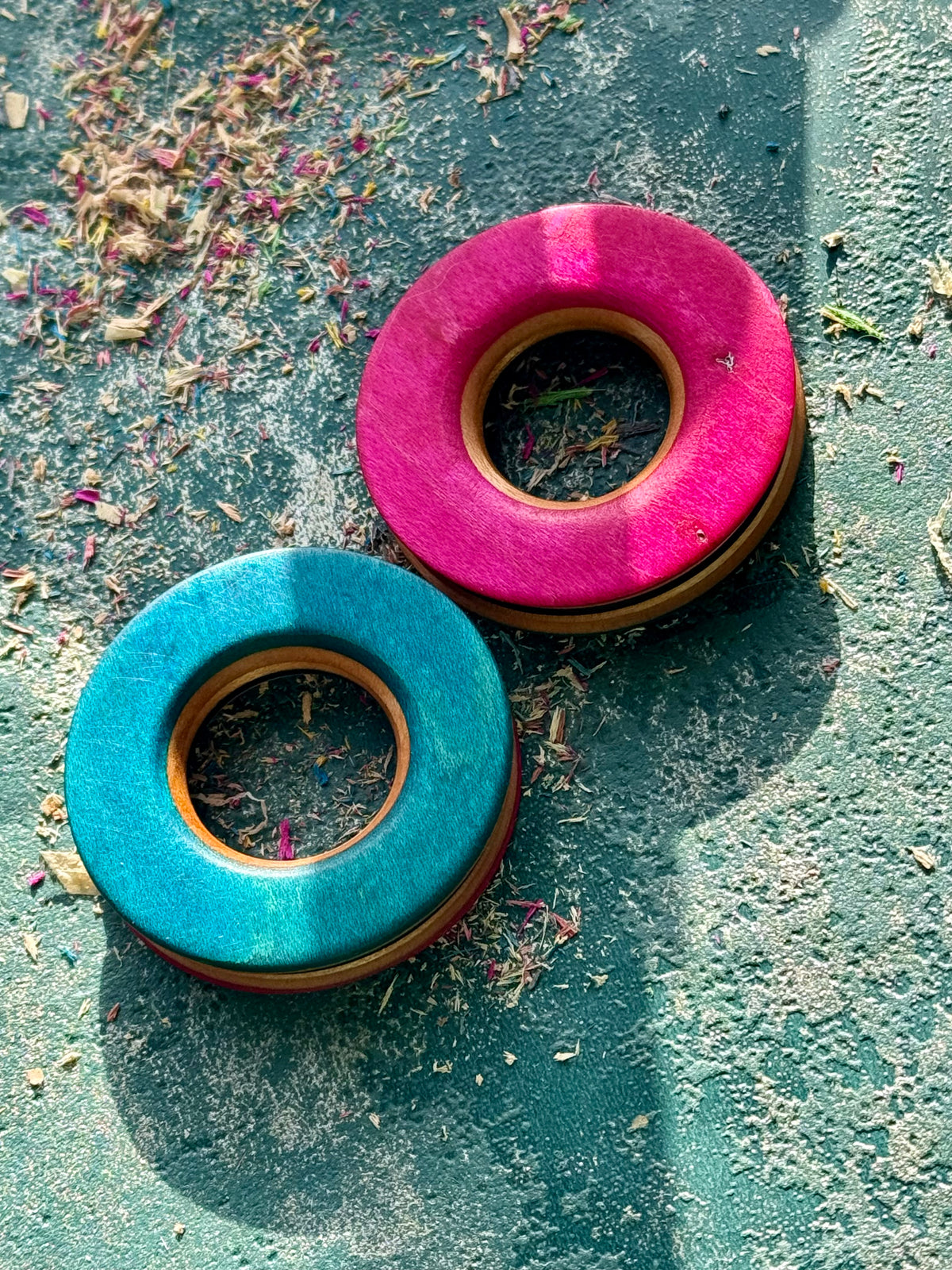 Pink and turquoise skateboard wood tunnels resting on a textured teal surface.