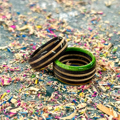 Handmade skateboard wood rings with black, natural and green tones, shown on a textured background.