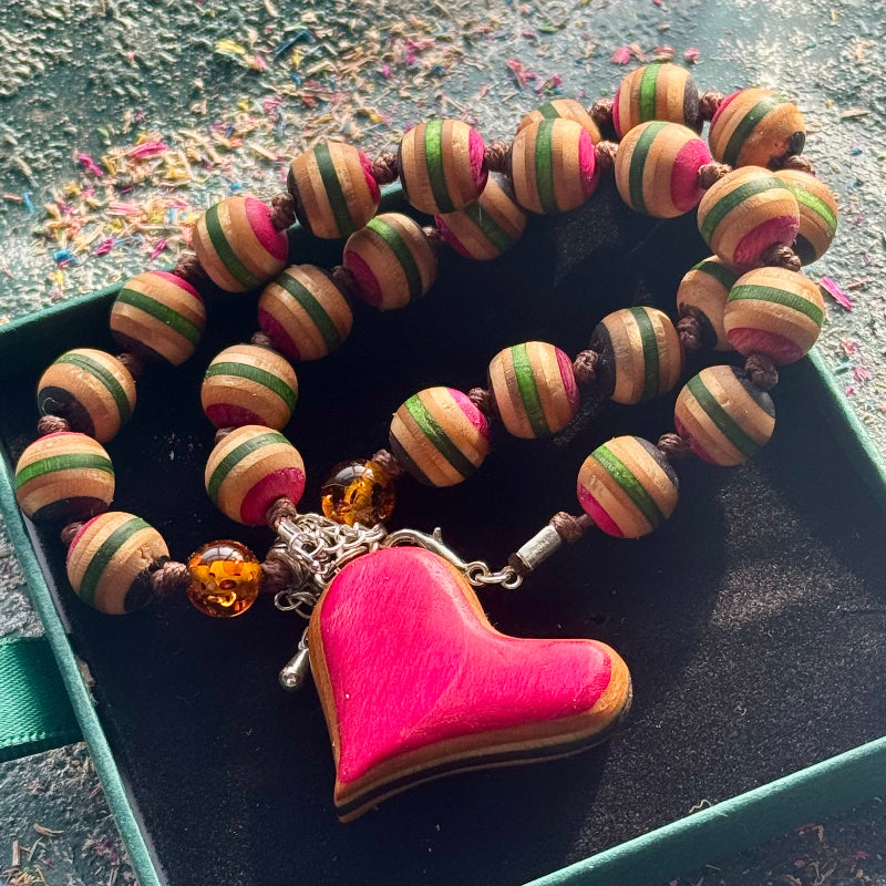 Close-up of a skateboard maple bead necklace with a pink heart pendant and amber beads.