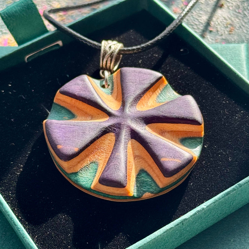 Close-up of a purple radial skateboard pendant in purple, orange and teal, in a green box.