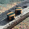 Teal and black double flare ear plugs at 16mm, layered skateboard maple around the wall.