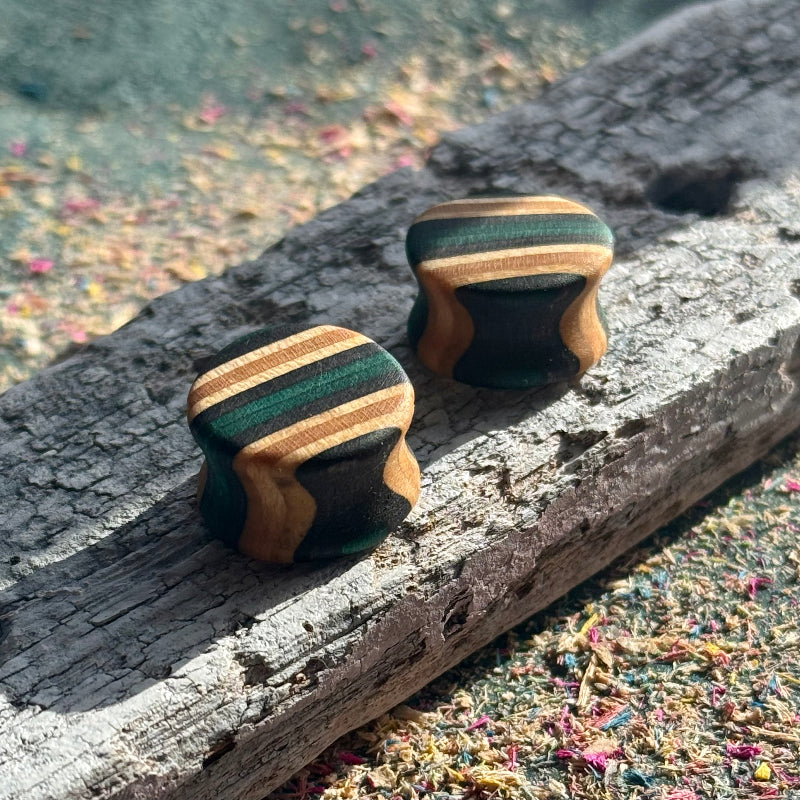 Teal and black double flare ear plugs at 16mm, layered skateboard maple around the wall.
