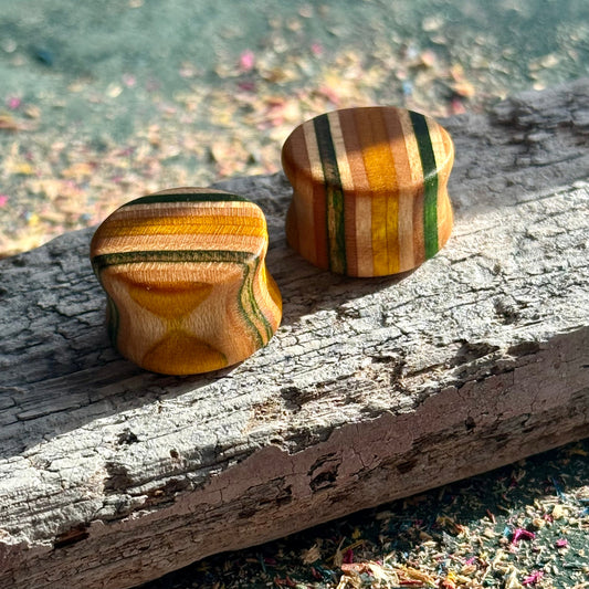 Green and Yellow Double Flare Wooden Ear Plugs 16mm resting on textured wood with natural light and colorful background particles