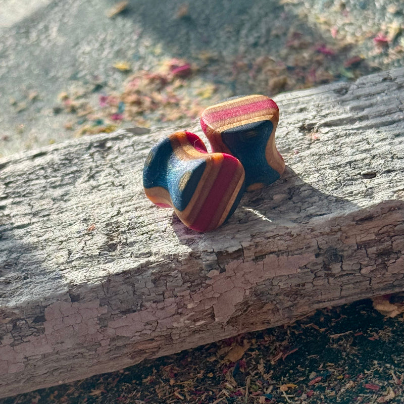 Pink and Blue Double Flare Wooden Ear Plugs 10mm resting on a piece of weathered wood outdoors in natural light