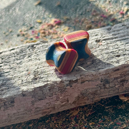 Pink and Blue Double Flare Wooden Ear Plugs 10mm resting on a piece of weathered wood outdoors in natural light